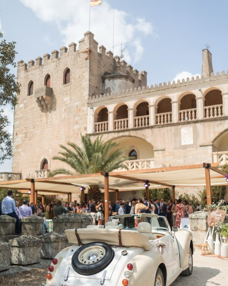 468841861_18320466001088528_5697901459317481465_n Recepción de invitados en un castillo con coche clásico blanco descapotable y decoración para evento elegante.