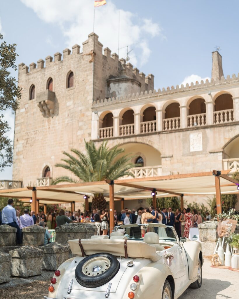 Recepción de invitados en un castillo con coche clásico blanco descapotable y decoración para evento elegante.