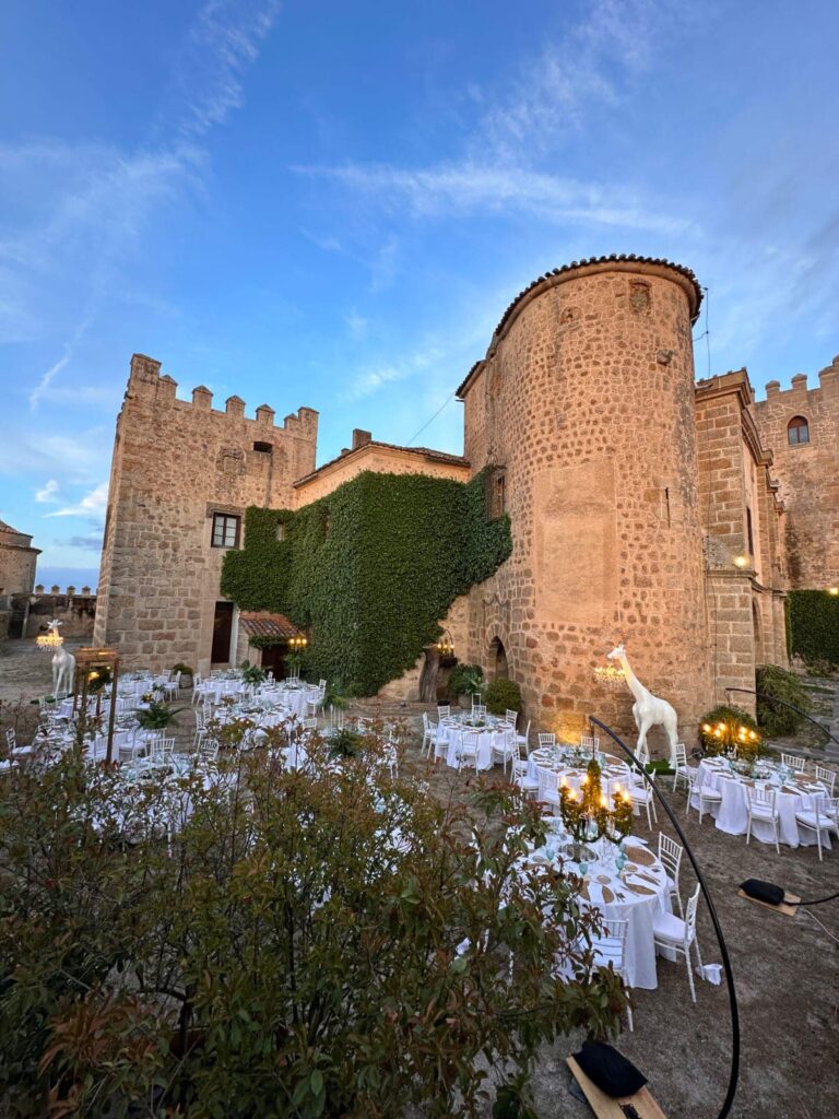 Vista panorámica de una celebración en exterior con mesas decoradas junto a castillo de piedra cubierto de hiedra.